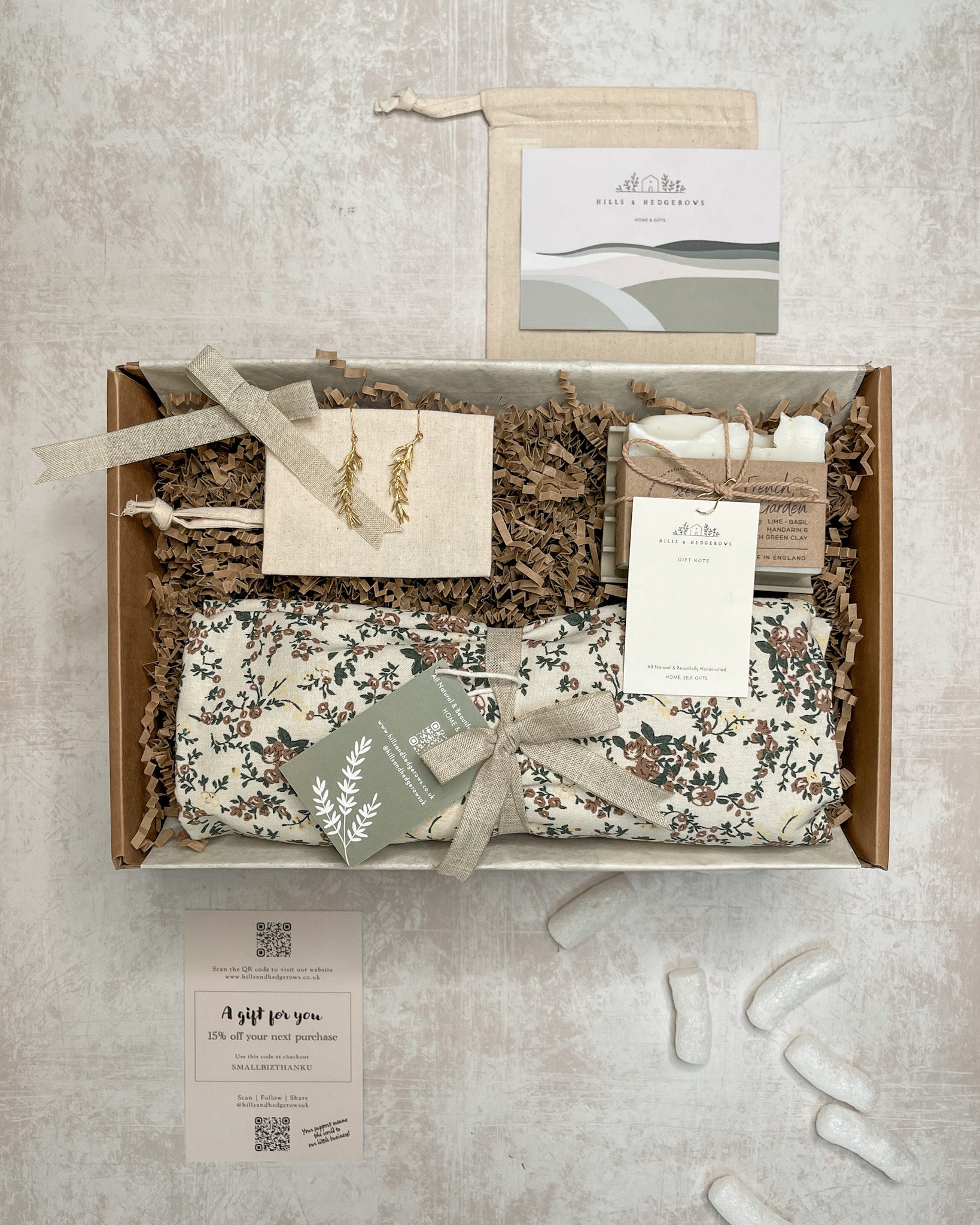 French Floral Garden Gift Set featuring a cream floral pinafore, rosemary sprig earrings, French garden soap, and concrete soap dish, perfect for bringing the essence of nature into your home.