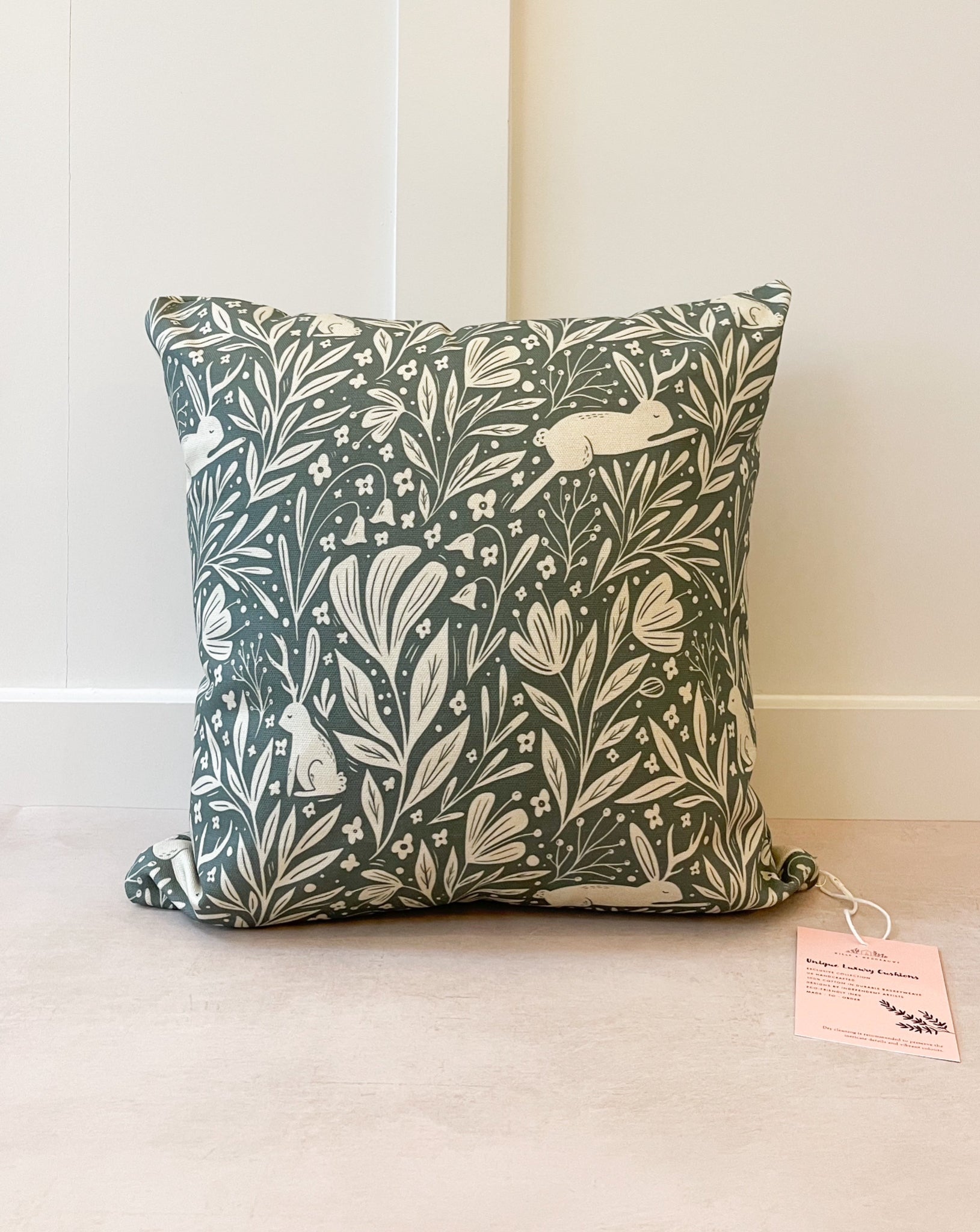 Botanical Cushion featuring an enchanting floral pattern with a leaping hare with one ear and one antler, set against a deep blue-green background with a cream foreground.