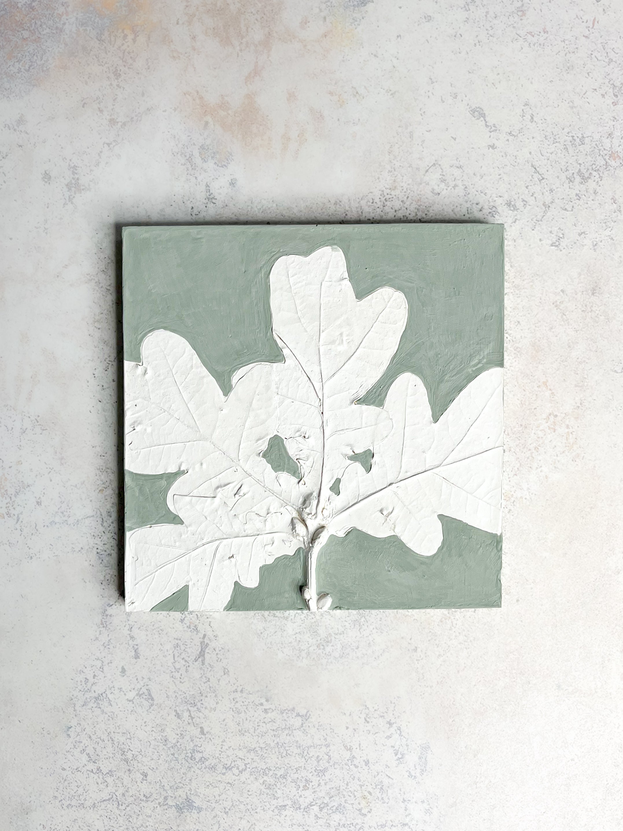 Handcrafted botanical relief tile featuring oak leaves, hand-painted in sage green, symbolising strength and resilience.