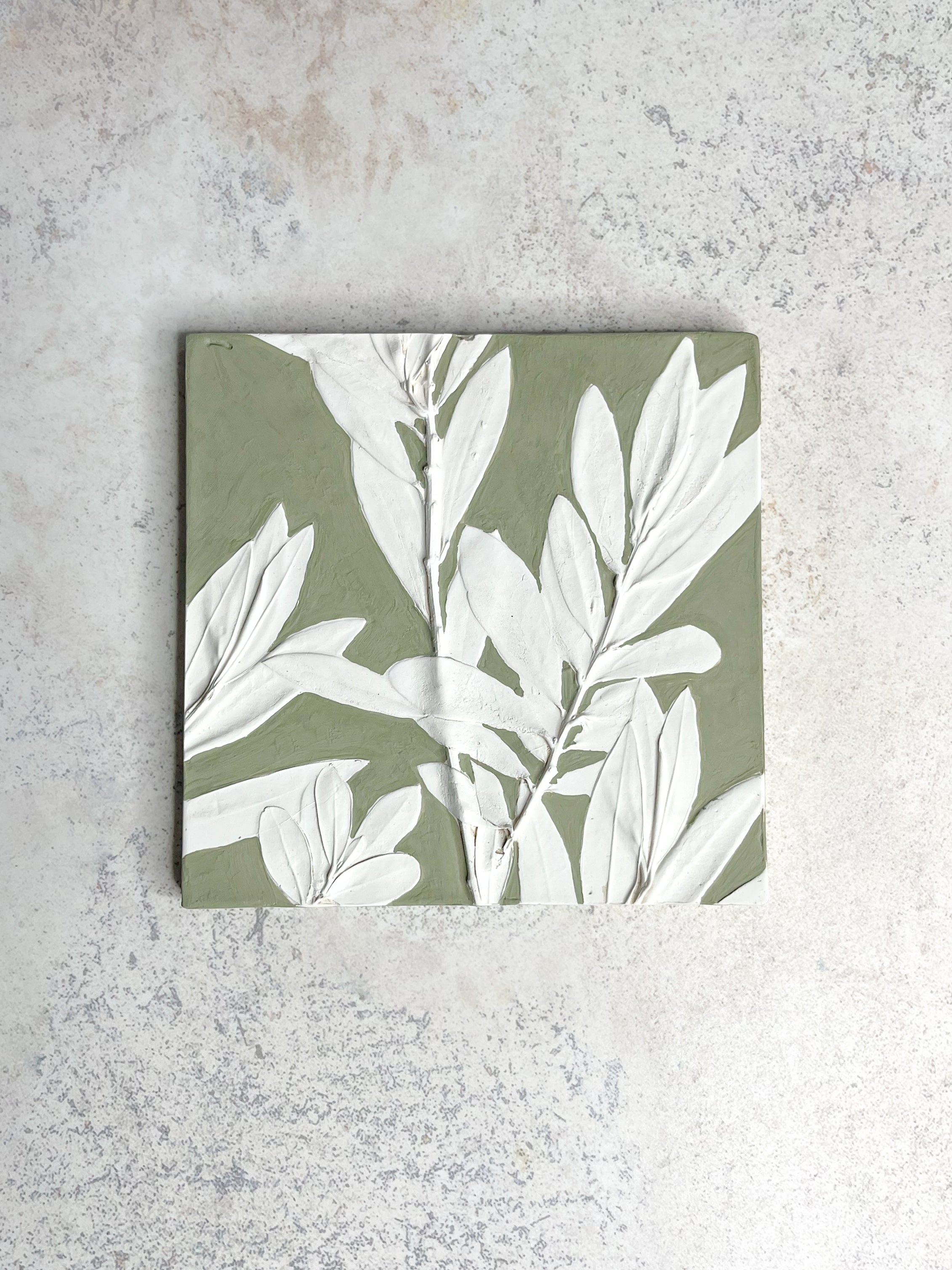 Handcrafted botanical relief tile featuring olive leaves, hand-painted in dusty green, symbolising peace and resilience