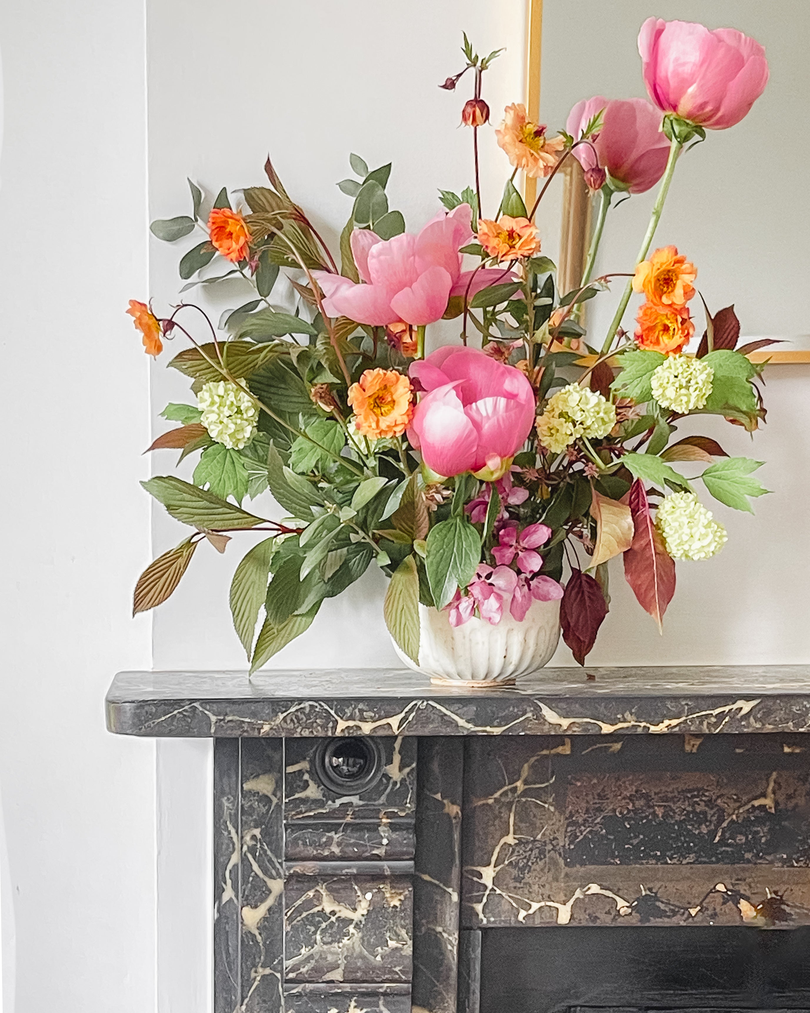 Period characterful fireplace mantle with ceramic ikebana bowl with fresh flowers arranged including pink peonies.