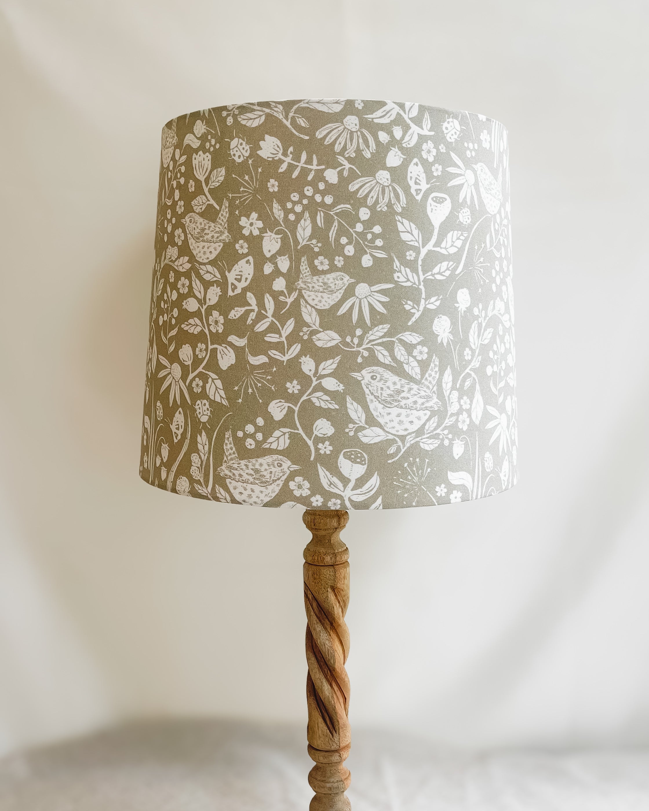 Wren's Hedgerow Lampshade with block print style wrens, wildflowers, and berries in soft white on a taupe background, handmade with linen and cotton, perfect for adding a rustic touch to home decor.